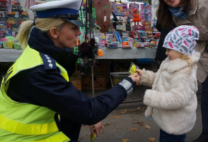 Zdjęcie policjantki podającej zawieszkę odblaskową dziecku